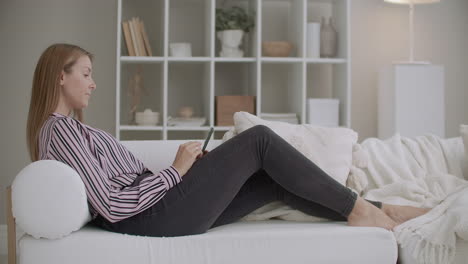 young-woman-is-resting-at-home-and-chatting-by-messages-in-smartphone-lying-on-couch-in-living-room